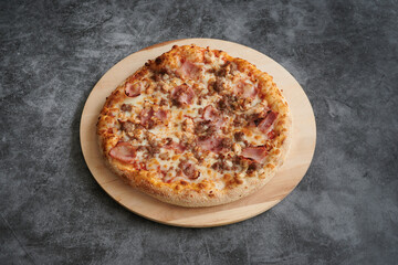 A pizza with ham and cheese on a wooden plate. The pizza is on a table