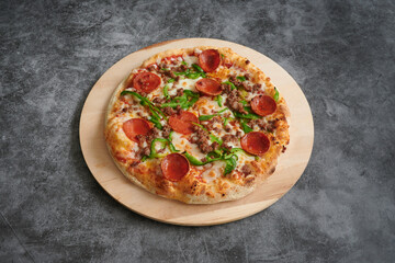 A pizza with pepperoni and green peppers on a wooden board. The pizza is cut into slices