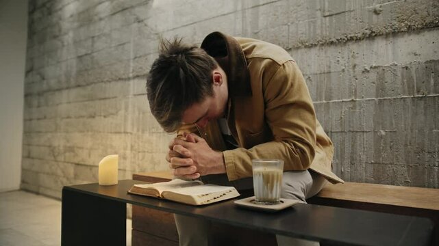 Man praying with Bible and candlelight
