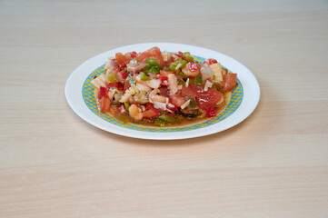 A plate of food with tomatoes and peppers on it. The plate is on a wooden table. The plate is white and blue