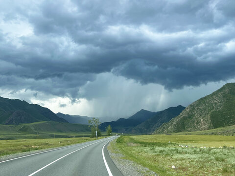 Dramatic rain clouds over mountain road in lush green landscape