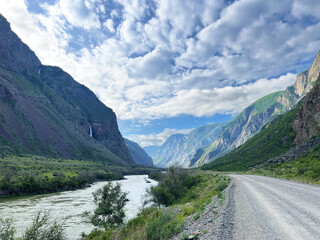 Naklejka premium Majestic mountain river valley on cloudy day with gravel road and lush greenery
