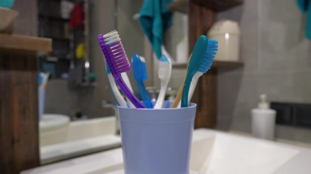 Many colorful toothbrushes in a glass on a turntable, in a bathroom, dental hygiene concept. Slow motion.