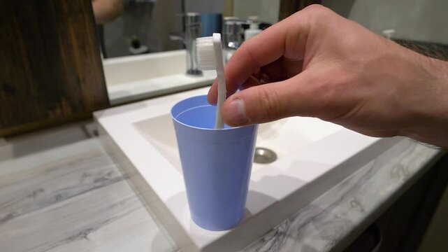 Close up, hand taking toothbrush, young man brushing teeth in bathroom at home. Slow motion