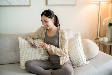 Happy asian woman using smartphone while sitting on sofa in living room
