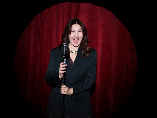 Adult woman in suit and a dress stands behind a microphone on stage and sing a song. Singer on stage