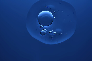 A neat drop of cosmetic serum on a dark blue background. Night skin care.