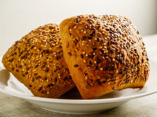 Three crusty rolls with seeds and grain in white bowl on simple light color table cloth. Fine bakery product made from high quality ingredients, Small bread.