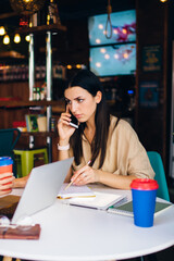 Serious women sitting in modern cafe with gadgets and coffee and working on project