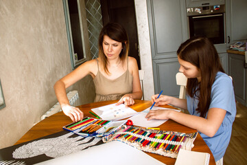 Fototapeta premium Mother and daughter laughing while drawing together, sharing tender moment. Touching scene of carefree childhood and qualitative parental involvement.