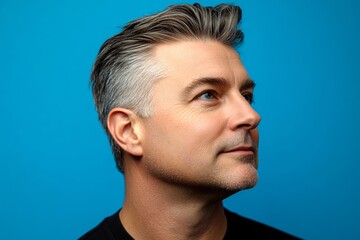Blue solid background. Conceptual art of style for aging men. Modish men's quiff haircut - midlife white man with hair. A man with expressive eyes and a joyful gaze.