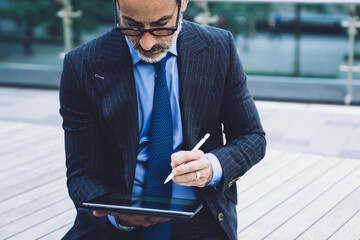 Adult male in business suit using tablet with stylus on bridge