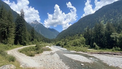 Serene river valley with dirt road, mountains, and lush forest under a sunny sky.