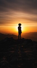 Obraz premium Silhouette of person standing on a mountain peak enjoying a vibrant sunset with orange sky and landscape views. Mountain top view.