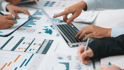 A diverse business team collaborates on a digital marketing strategy. Laptops and documents filled with data, charts, and graphs fill the modern office space. SACTR