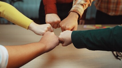 A group of diverse individuals showcases teamwork through a fist bump gesture, symbolizing unity and support in a collaborative office environment. SACTR