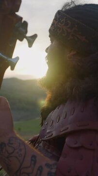 Obese man in ethnic clothes plays igil sitting in mountain valley at sunrise close side view. Siberian folks art and lifestyle. Hobby and leisure