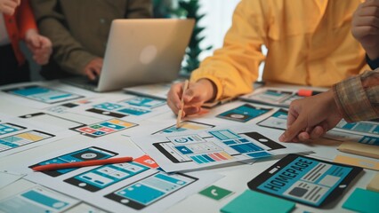 A diverse team collaborates on innovative design concepts for user-friendly mobile applications, surrounded by sketches, laptops, and brainstorming tools in a lively office. SACTR