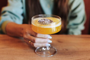 Elegant cocktail with foam. Woman holding glass. Refreshing drink served. Passion fruit garnish....