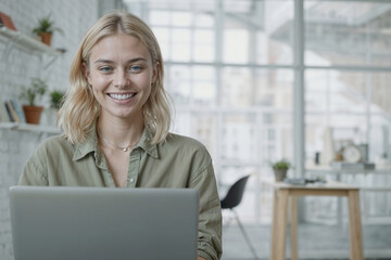 Portrait of beautiful blogger woman is sitting at a desk with a laptop in front of her, she is smiling and looking on camera