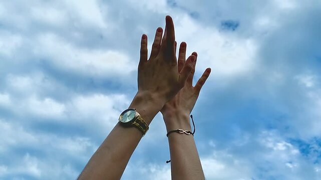 Close-up shot of hands reaching up against a bright blue sky, freedom and hope concept