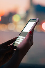 Smartphone with blank screen in female hands on blurred night city background