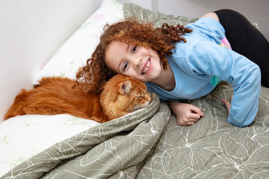 Happy girl playing with maine coon cat on bed in bedroom