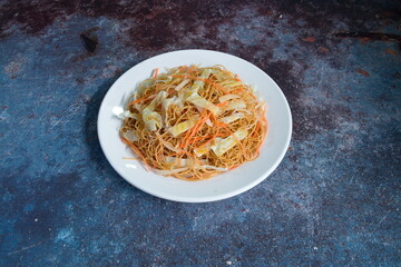 A plate of noodles with carrots on top. The plate is white and the noodles are orange