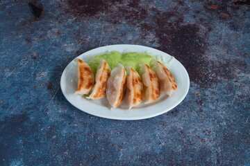 A plate of dumplings with a green leaf on top. There are six dumplings on the plate
