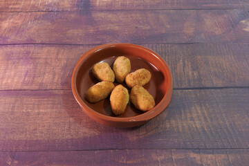 A bowl of fried food with six pieces of food in it. The bowl is brown and made of ceramic