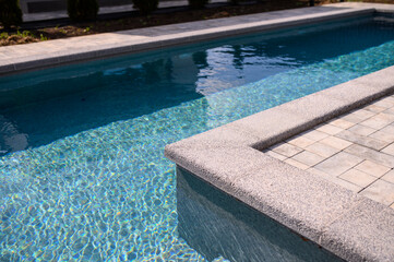 L-shaped pool is finished with a gray border stone. Clear blue water in the pool. Relaxing in the...