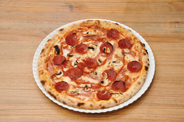 A pizza with pepperoni and mushrooms on a white plate. The pizza is sitting on a wooden table