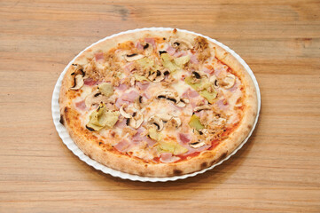 A pizza with mushrooms and ham on it. It is on a white plate. The pizza is on a wooden table