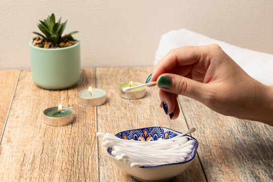 una mano de mujer tomando un hisopos, bastoncillos o cotonetes de un posillo de cer&aacute;mica azul, entorno tranquilidad y velas