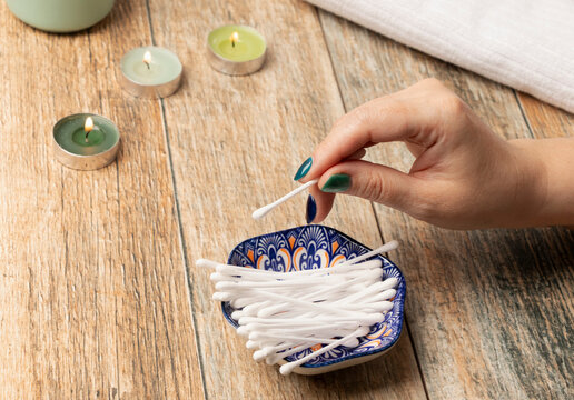 una mano de mujer tomando un hisopos, bastoncillos o cotonetes de un posillo de cer&aacute;mica azul, entorno tranquilidad y velas