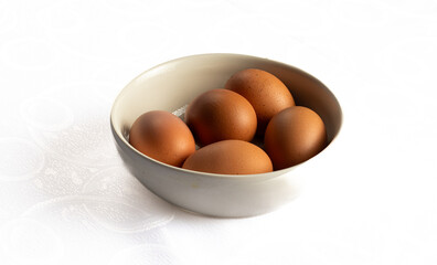 Five brown eggs in a white bowl on a white background.