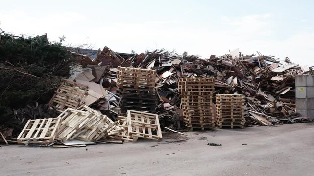 Piles of wooden pallets and construction debris including boards, branches, and panel fragments at an outdoor waste sorting or recycling facility.
