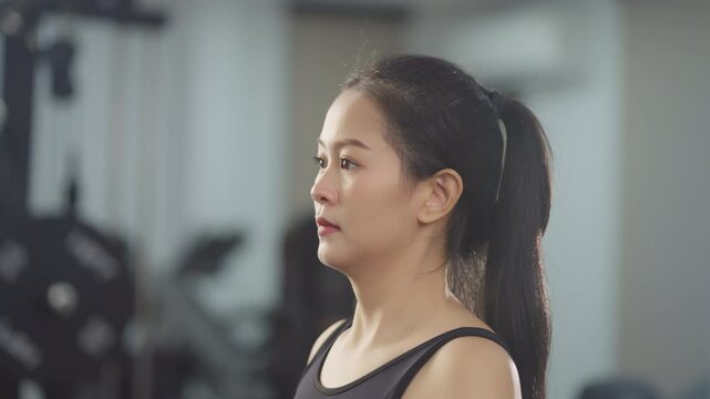 Focused asian woman lifting dumbbells for shoulder training, performing lateral raise exercise in gym, wearing black activewear and maintaining good form