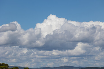 Bright white cumulus clouds drifting across blue sky over hills
