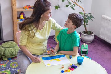 Art Therapy Session: Adult and Child Painting Together in Supportive Environment. Mom helps her son...