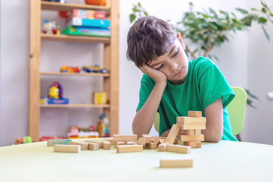 Child Showing Frustration During Learning Activity with Wooden Blocks. Difficulty with task persistence in children with autism or dyspraxia. Sensory or cognitive overload during educational tasks. 