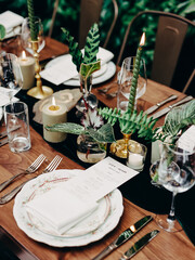 Elegant dinner table setup with candles, greenery, and stylish dinnerware amidst a lush setting