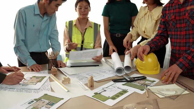 Smart architect and safety engineer discussion about building blueprint on table with architectural document, measurement tools and wooden block scatter around at modern office. Closeup. Delineation.