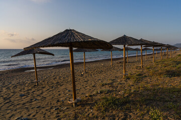 Picturesque seascape. Straw beach umbrellas against sunset sky evoke feeling of relaxation, serenity and romantic ending of summer day by sea.
