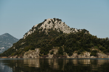 Scenic view of Montenegro mountainous landscape reflecting on the calm waters of Skadar Lake. Rugged limestone peaks and dense forests create a tranquil and cinematic atmosphere.