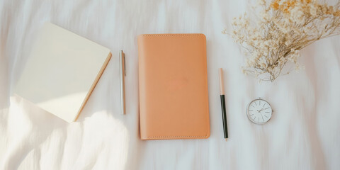 Fototapeta premium Elegant flat lay of notebook, pen, diary, and clock on white fabric with dried flowers