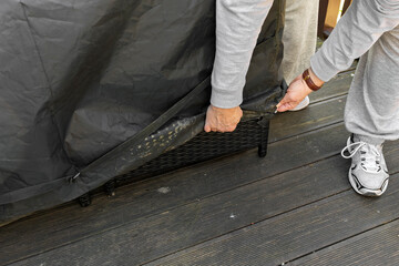 A man removes a black winter cover from a patio table on a wooden deck. Illustrates uncovering...