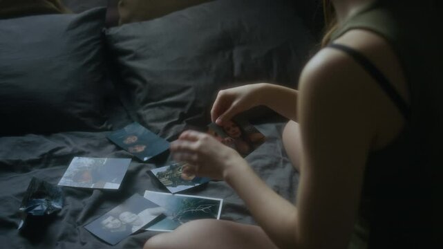 Over-shoulder shot of unrecognizable woman sitting in bed and looking through pictures with boyfriend, tearing one photo out of harsh pain from breakup