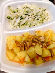 Savory chicken and potato dish served with fresh cucumber and cabbage salad in a takeout container healthy eating concept