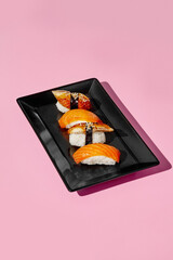 Delicious sushi pieces with salmon and eel on black plate and pink background